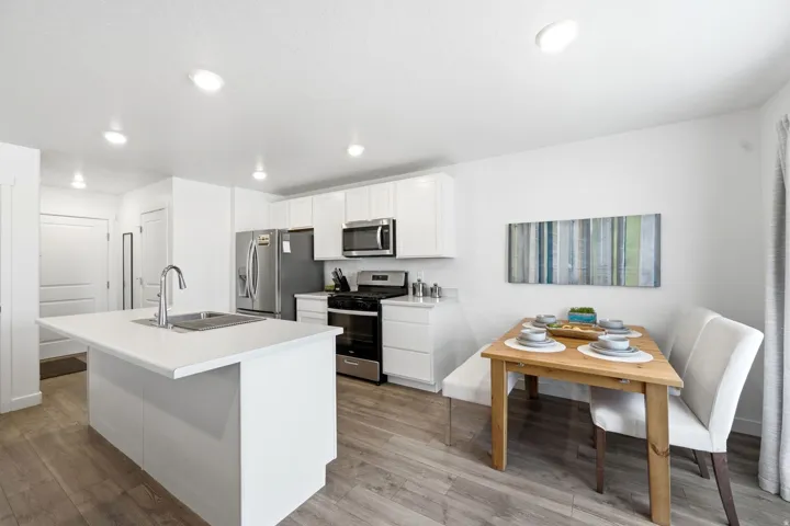 Kitchen featuring a white island with an undermount sink, stainless steel appliances, white cabinetry, wood-finish flooring, and recessed lighting