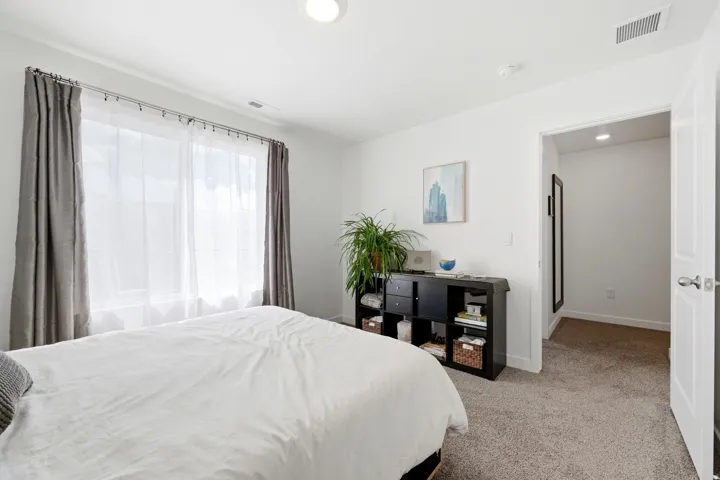 Bright bedroom featuring a large window with sheer and blackout curtains, recessed ceiling lighting, and neutral carpeting