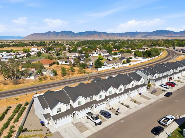 New construction townhome development featuring light-colored siding, dark shingle roofs, individual garages, and mountain scenery in the background
