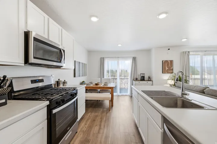 Modern kitchen featuring white cabinetry, stainless steel appliances, wood-finish flooring, recessed lighting, and a kitchen island with an integrated sink