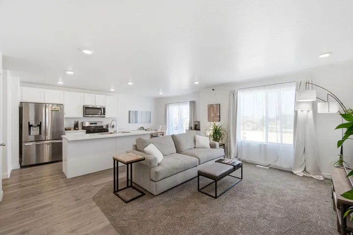 Open-concept living area featuring a kitchen with stainless steel appliances, white cabinetry, and a peninsula with a light-toned countertop