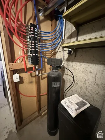 PEX manifold system with red and blue piping, water softener, and water filtration system against a concrete wall