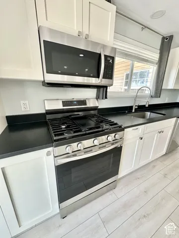 Modern kitchen featuring white shaker cabinetry, dark countertops, stainless steel appliances, and wood-finish flooring