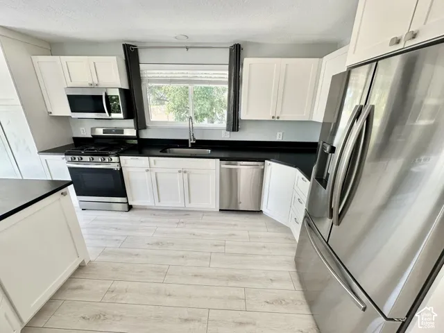 Kitchen featuring wood-finish flooring, white cabinetry, dark countertops, and stainless steel appliances including a refrigerator, range, microwave, and dishwasher