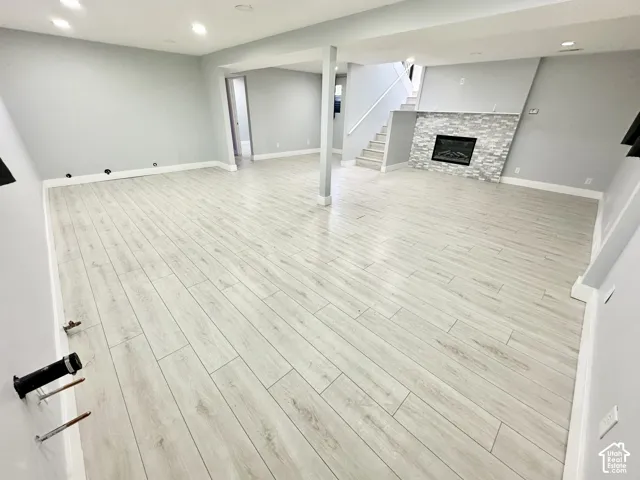 Spacious open-concept room featuring light wood-finish flooring, a contemporary electric fireplace with a stacked stone facade, recessed lighting, and crisp white baseboards