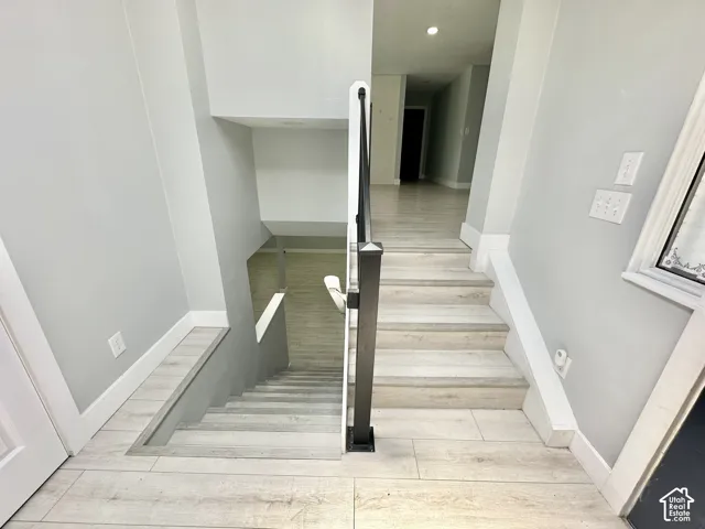 Staircase with light wood-finish flooring and a black metal newel post