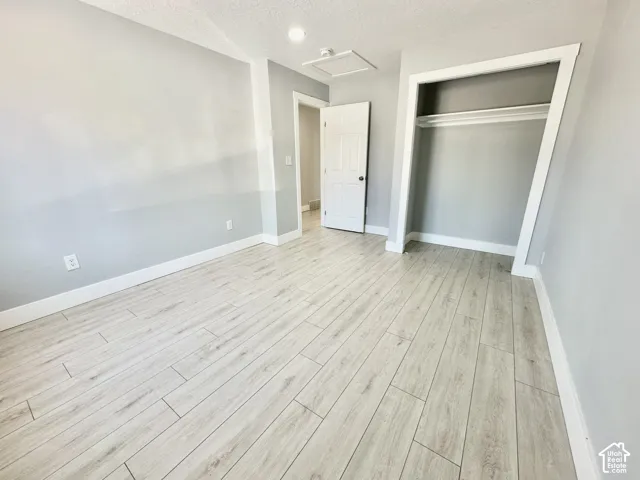 Light wood-finish flooring complements neutral gray walls, featuring a built-in closet with hanging rod, white trim, and a white interior door
