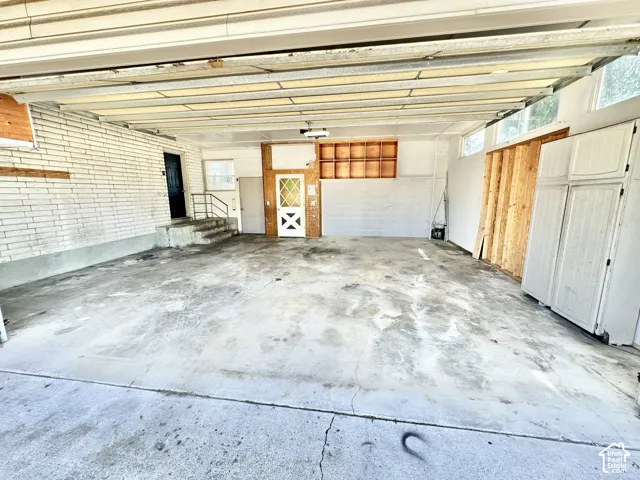 Spacious carport featuring a concrete floor, white brick wall, and multiple entry points