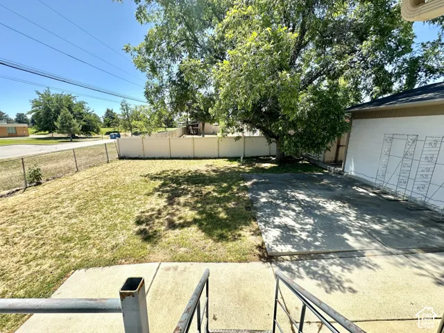 Expansive backyard featuring a large tree providing ample shade, a concrete patio area, and a white privacy fence