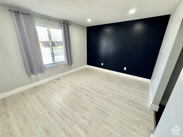 Spacious room featuring light wood-finish flooring, a prominent accent wall, recessed lighting, white baseboards, and a window with blinds