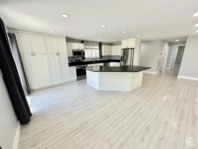 Kitchen featuring a multi-sided island with a dark countertop, white cabinetry with silver-toned hardware, stainless steel appliances, and recessed lighting