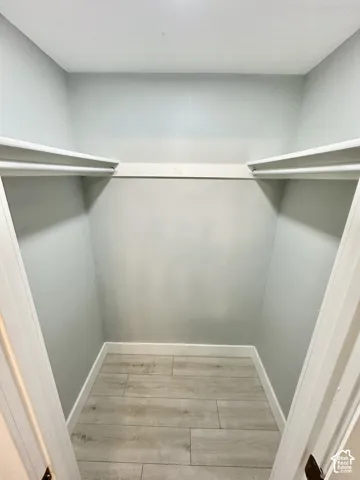 Walk-in closet with light gray walls, wood-finish tile flooring, white baseboards, and built-in shelving with hanging rods