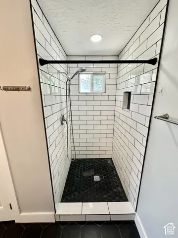 Shower enclosure featuring subway tile walls, black hexagonal floor tile, a built-in shower niche, and a window