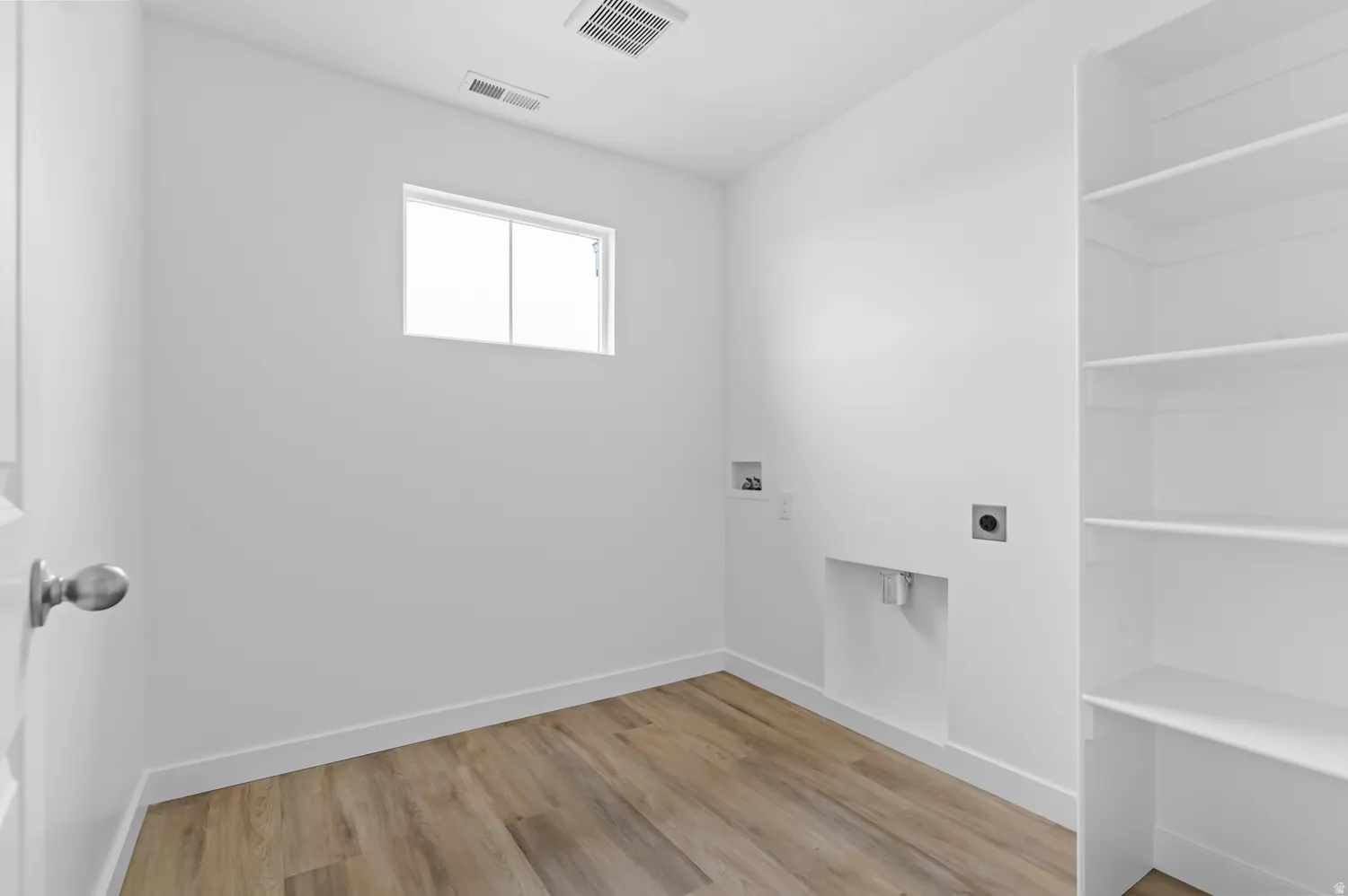 Utility room with wood-finish flooring, built-in shelving, and a single window