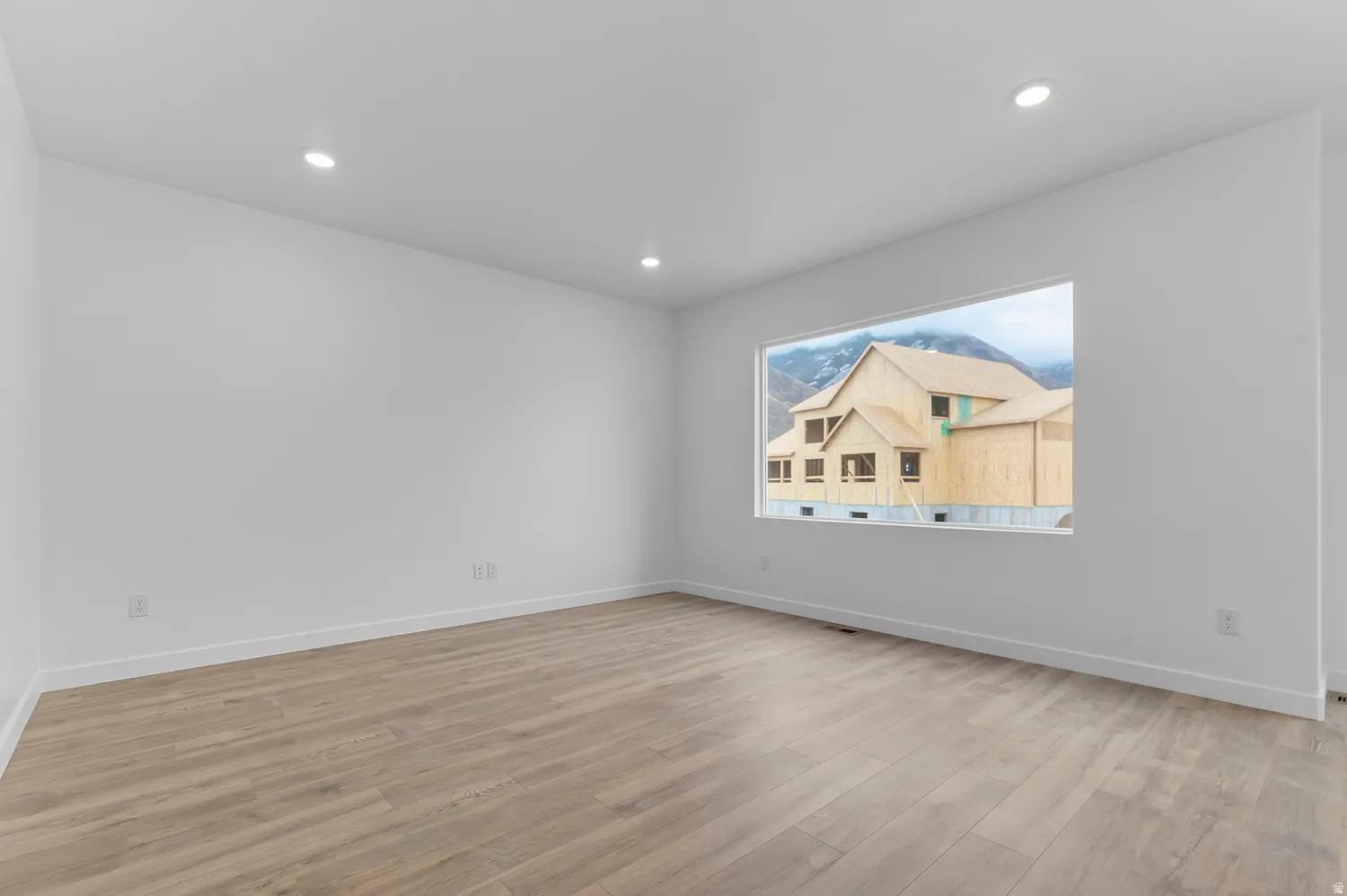 Spacious room featuring light wood-finish flooring, recessed lighting, and a wide window