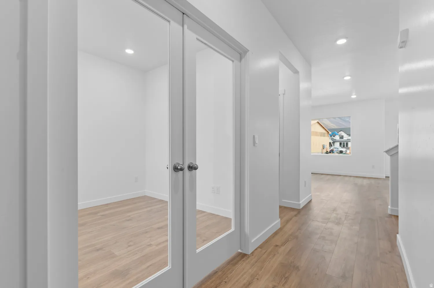 Glass-paneled double doors framing a versatile room with wood-finish flooring