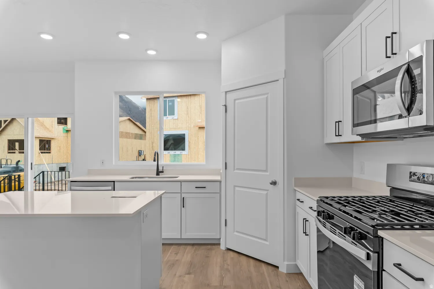 Modern kitchen featuring a central island, white cabinetry with matte black hardware, integrated stainless steel appliances, and wood-finish flooring