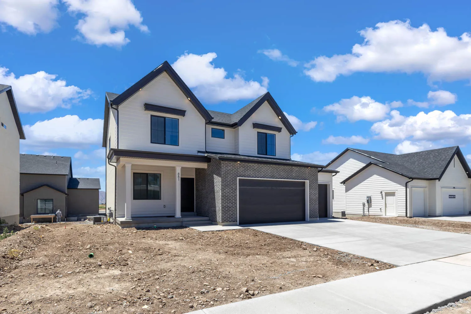 Modern two-story residence featuring white siding, dark trim, a covered entry with columns, and an integrated garage with a dark door, complemented by a concrete driveway