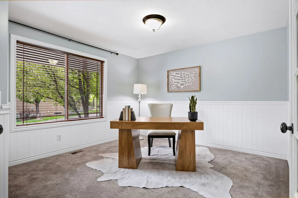 Bright room featuring a large window with horizontal blinds, white beadboard wainscoting, light blue walls, and carpeting