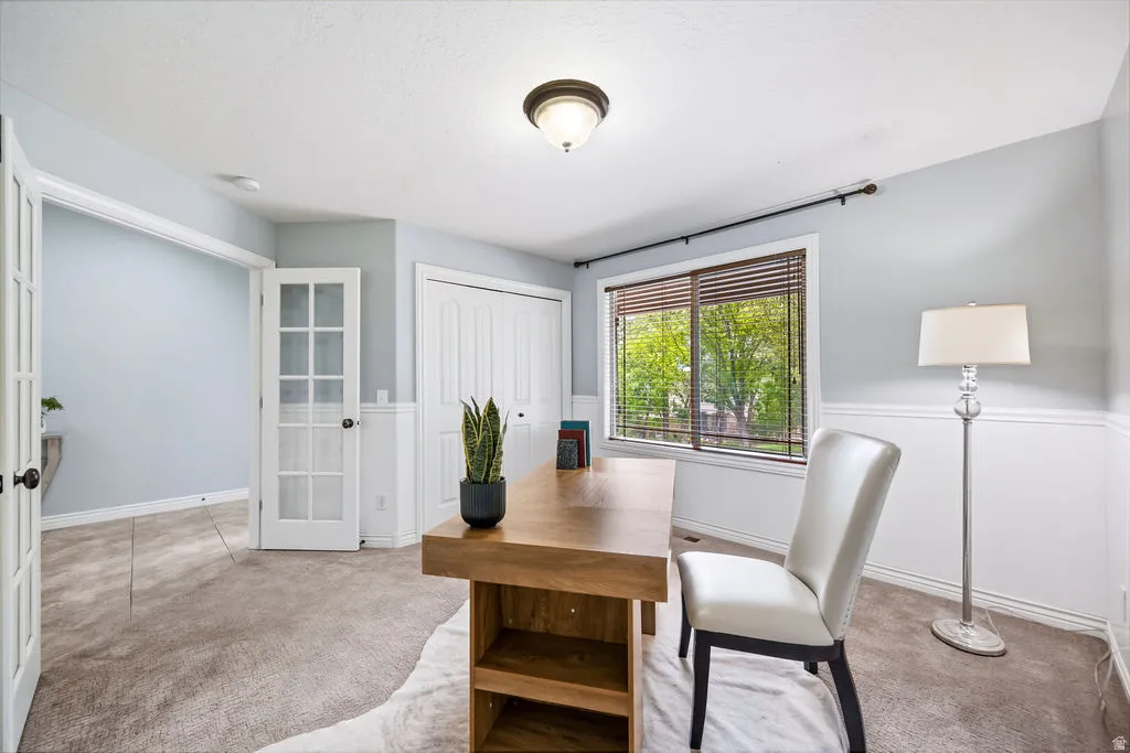 Carpeted room featuring a large window with horizontal blinds, built-in closet with bifold doors, and wainscoting