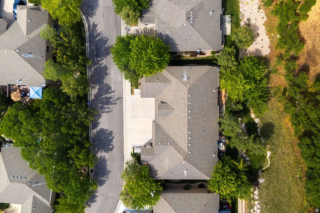 Aerial perspective showcasing a residential property with a gray shingled roof, a paved driveway, and mature landscaping