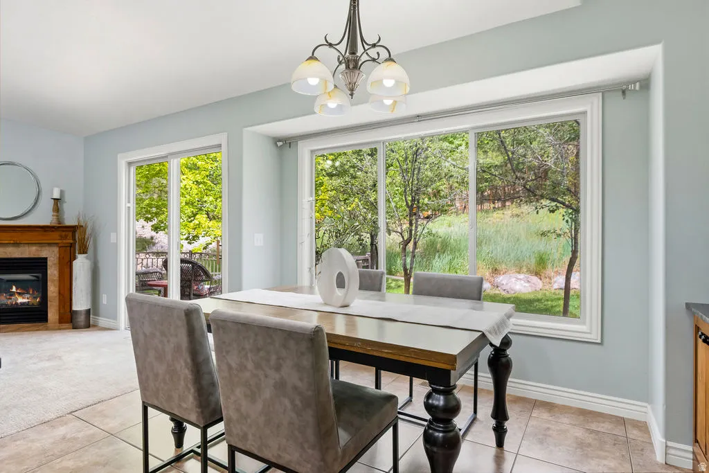 Dining area featuring a large picture window, a sliding glass door, tiled flooring, a fireplace with a wood mantel, and a multi-light chandelier