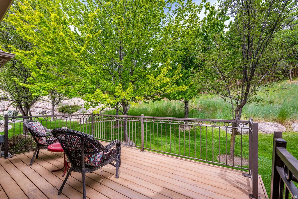 Expansive wood-finish deck with a decorative metal railing overlooking a lush green space and mature trees