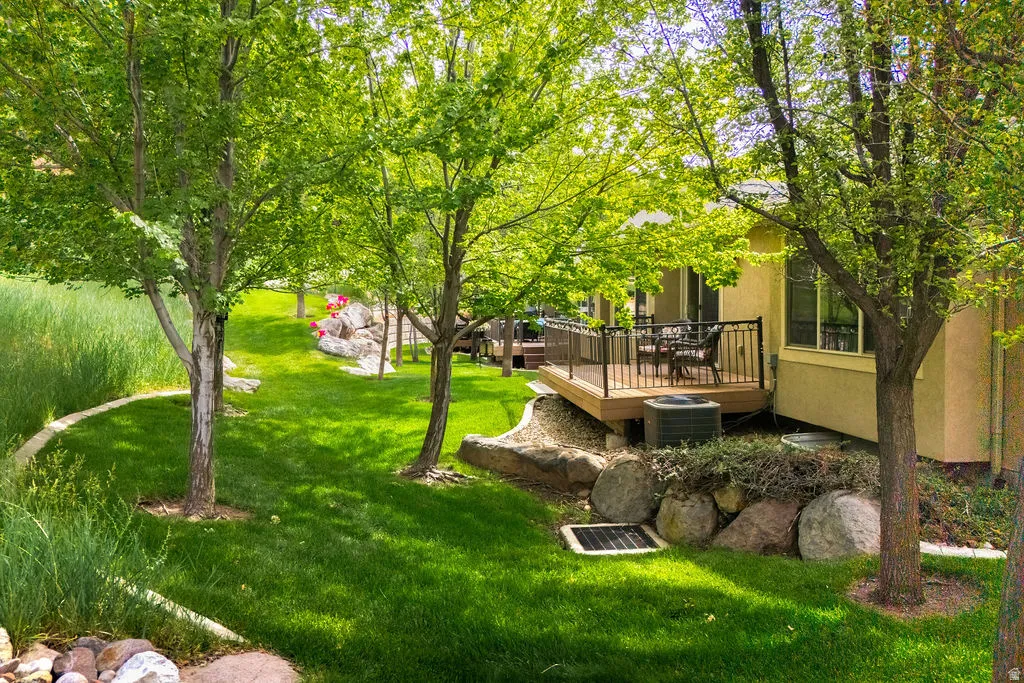 Exterior deck with black metal railing, flanked by mature trees and a manicured lawn