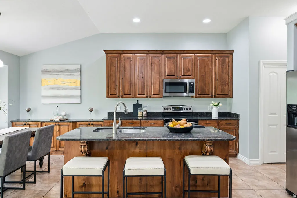 Kitchen featuring a central island with an integrated sink, dark countertops, wood cabinetry, and stainless steel appliances