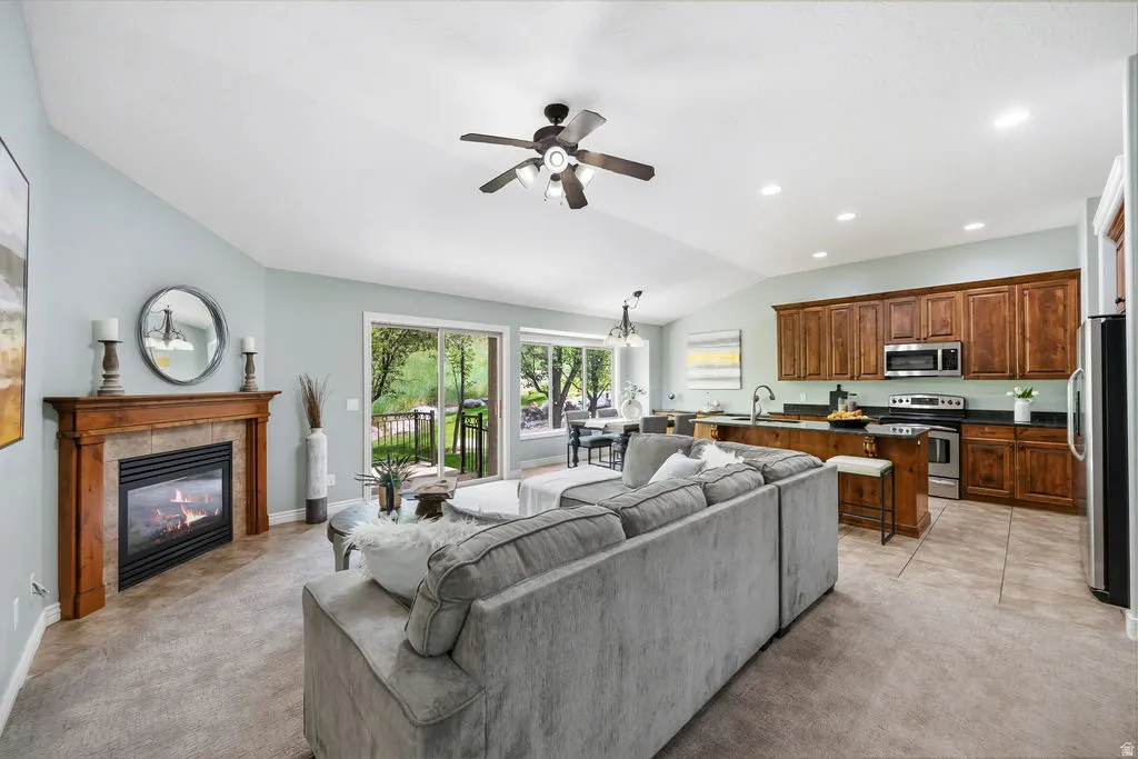 Spacious open-concept living area featuring a fireplace with a wood mantle and tile surround, vaulted ceiling with a ceiling fan, and sliding glass doors opening to the outdoors