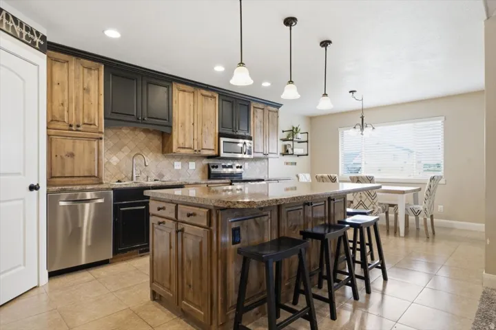 Kitchen featuring an oversized island with a stone countertop, a tile backsplash, stainless steel appliances, and two-tone cabinetry
