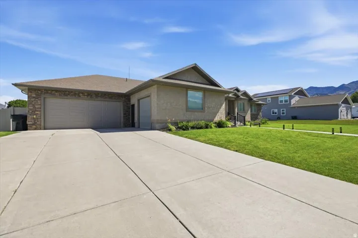 Contemporary ranch-style residence featuring a textured stucco exterior, stone facade accents, and a dual garage