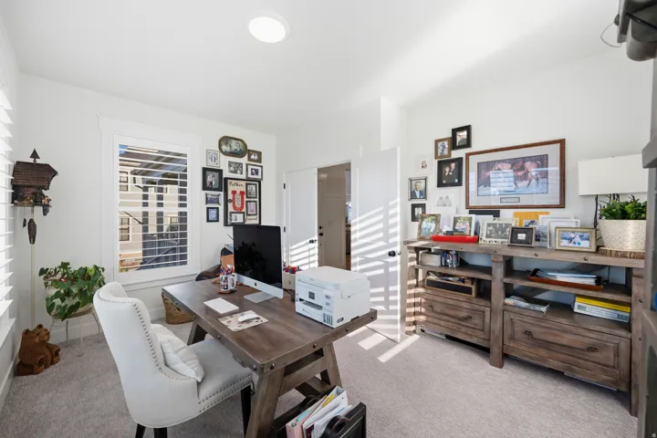 Bright room featuring a window with white louvered shutters, light gray carpet flooring, a white ceiling with recessed lighting, and a white interior door