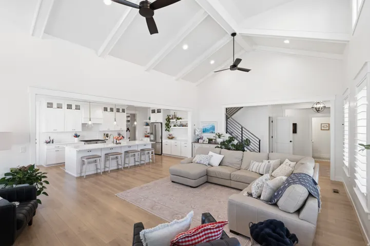 Bright, open-concept living area featuring a vaulted ceiling with exposed beams, wood-finish flooring, and white plantation shutters
