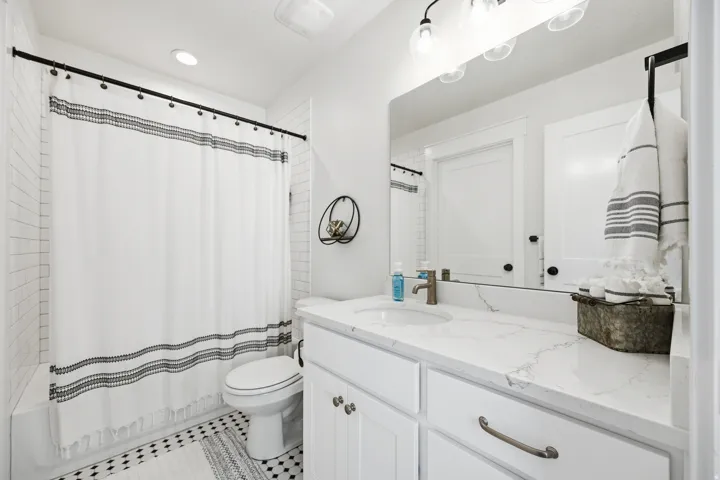 Bathroom featuring a white subway tile surround, black and white patterned floor tile, a white vanity with shaker-style cabinetry, and a white countertop with integrated sink