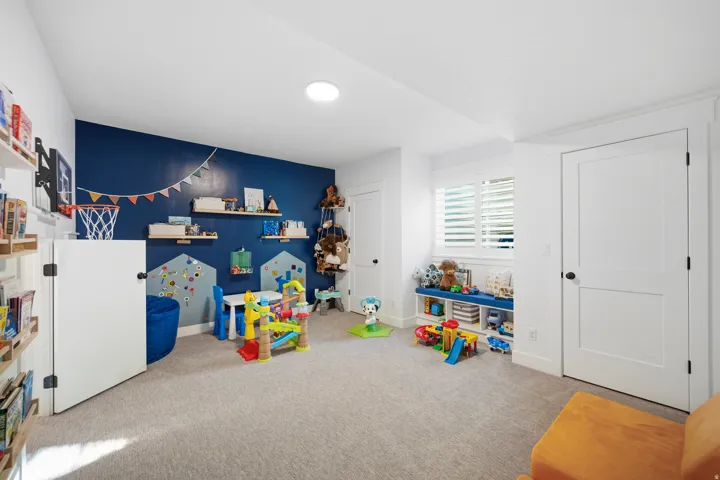 Spacious room featuring carpeting, a deep blue accent wall with built-in shelving, white plantation shutters, and recessed lighting
