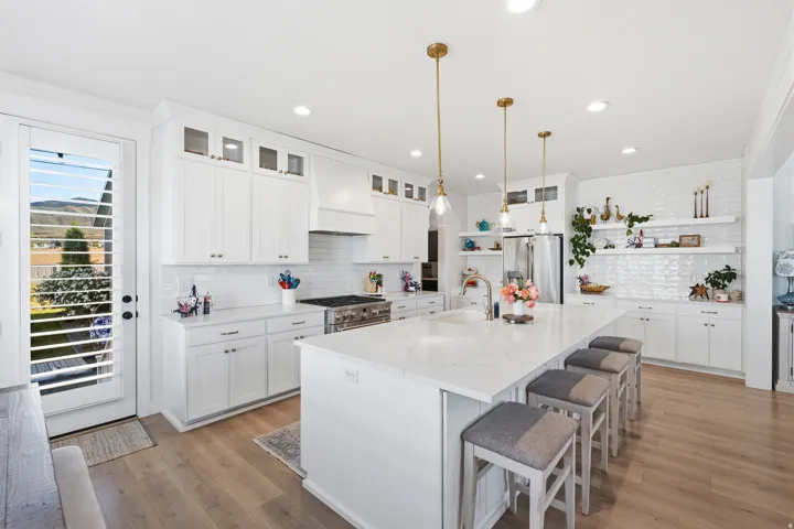 Spacious kitchen featuring an expansive island with seating, white shaker cabinetry, stainless steel appliances, wood-finish flooring, and a white subway tile backsplash