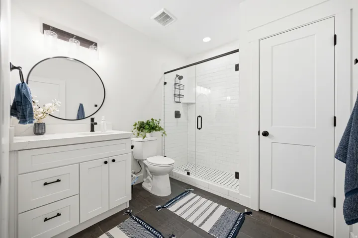 Bathroom featuring a white vanity with quartz countertop, black hardware, and a round black-framed mirror