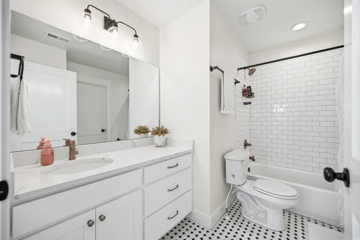 Bathroom featuring a single vanity with stone-finish countertop, white cabinetry, a built-in tub with subway tile surround, and black and white patterned floor tile