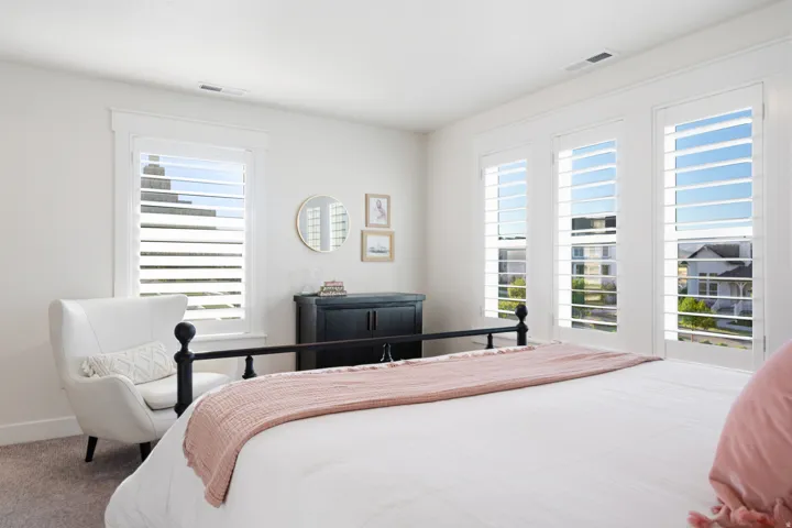 Bright room featuring multiple windows with louvered shutters, light-colored walls, and a dark wood dresser