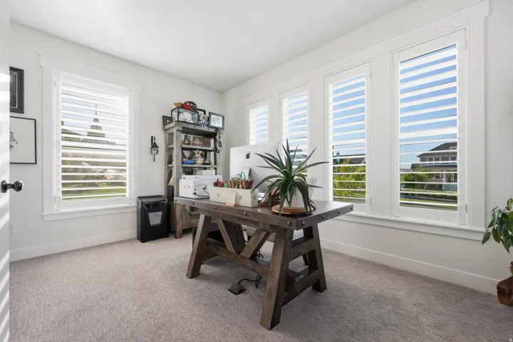 Bright room with multiple windows featuring white plantation shutters, neutral carpeting, and white trim