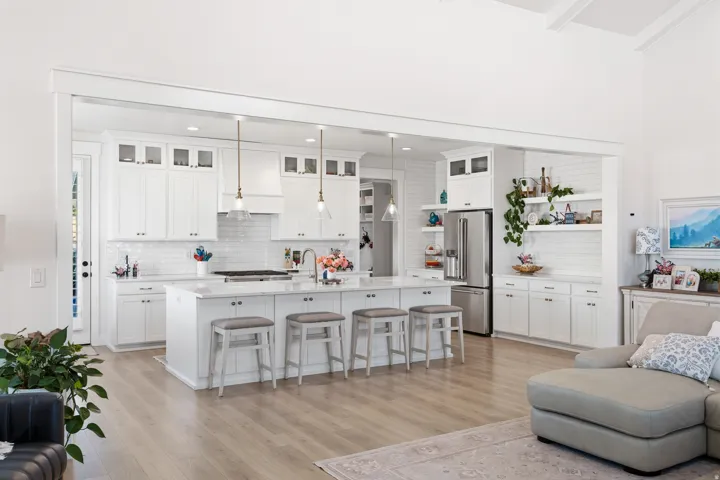 Open-concept kitchen featuring white shaker cabinetry, an expansive central island with seating, pendant lighting, and wood-finish flooring