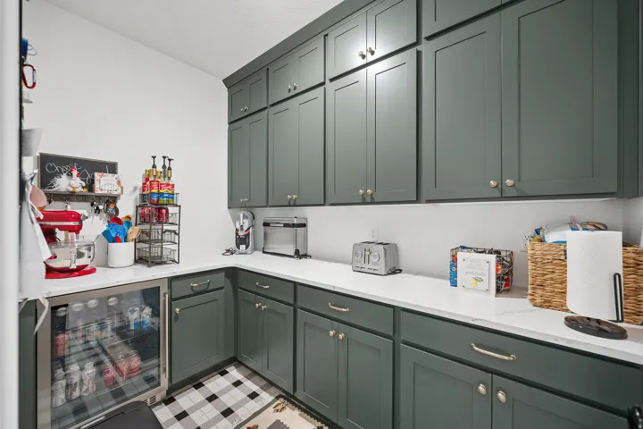 Spacious pantry featuring extensive green shaker cabinetry, white quartz countertops, black and white checkered flooring, a built-in beverage refrigerator, and ample storage