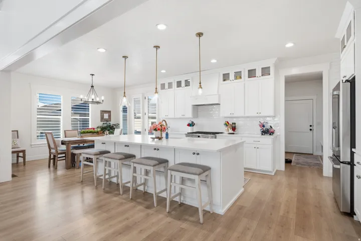 Spacious kitchen featuring an expansive central island with seating, white shaker cabinetry, wood-finish flooring, recessed lighting, and stainless steel appliances