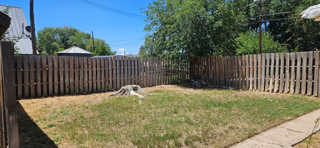 Fenced backyard area featuring a wood privacy fence, a mature tree providing natural shade, and a concrete pathway