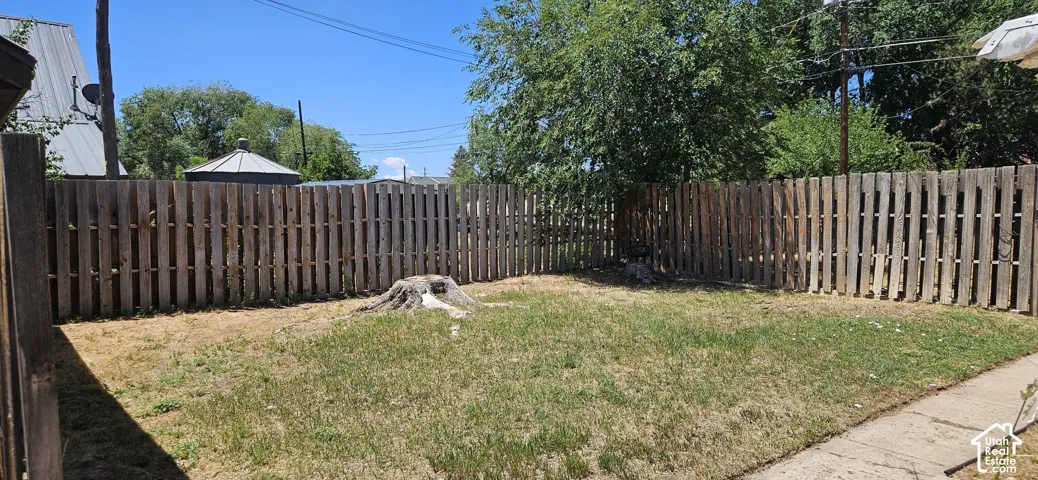 Fenced backyard area featuring a wood privacy fence, a mature tree providing natural shade, and a concrete pathway