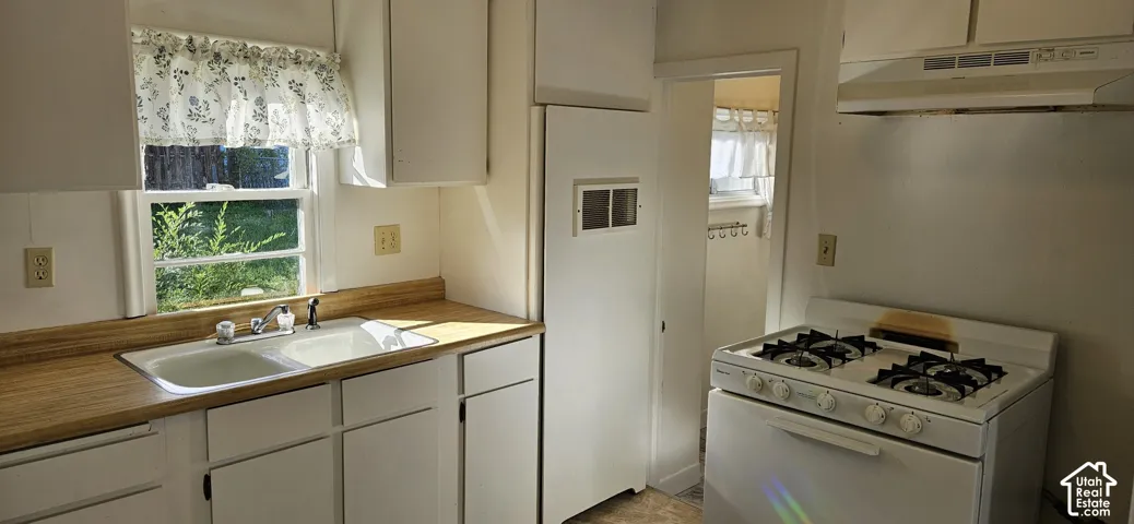 Kitchen featuring white cabinetry, light-toned laminate countertops, a double-basin sink with a chrome faucet, and a four-burner gas range with an integrated hood