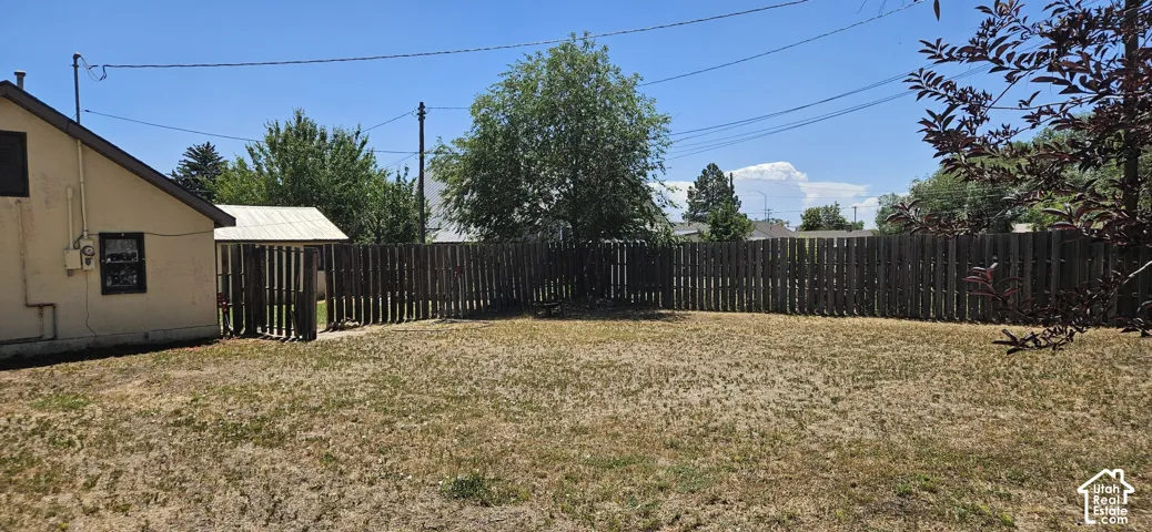 Expansive outdoor space featuring a full perimeter privacy fence, a mature shade tree, and a side access gate