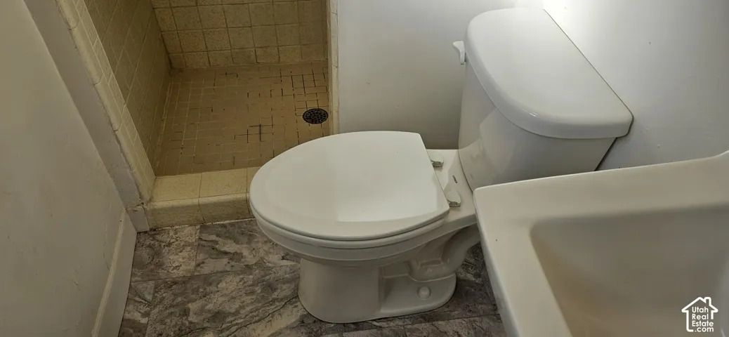 Bathroom featuring a walk-in shower with tiled walls and flooring, white porcelain toilet, and stone-patterned vinyl flooring