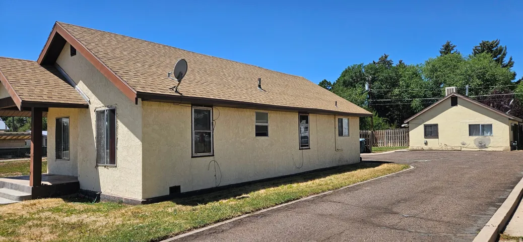 Stucco exterior property with a brown shingle roof and multiple windows